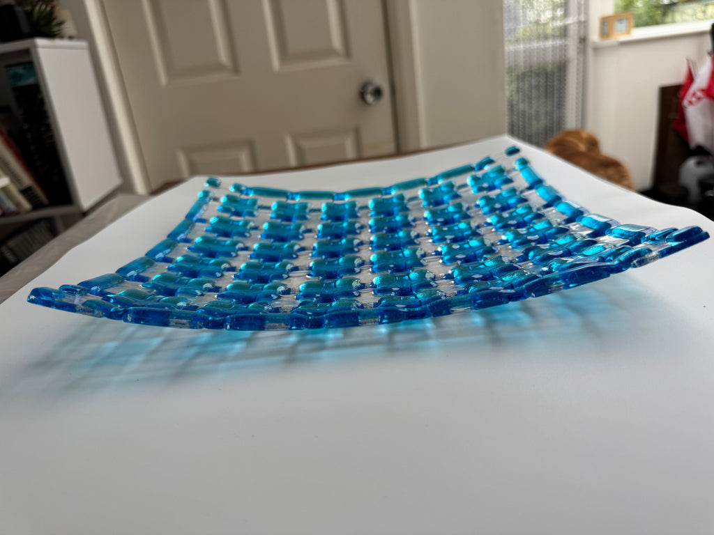 A translucent blue and clear glass bowl with a grid-like pattern, resting on a white table in a home setting with a door and window in the background.